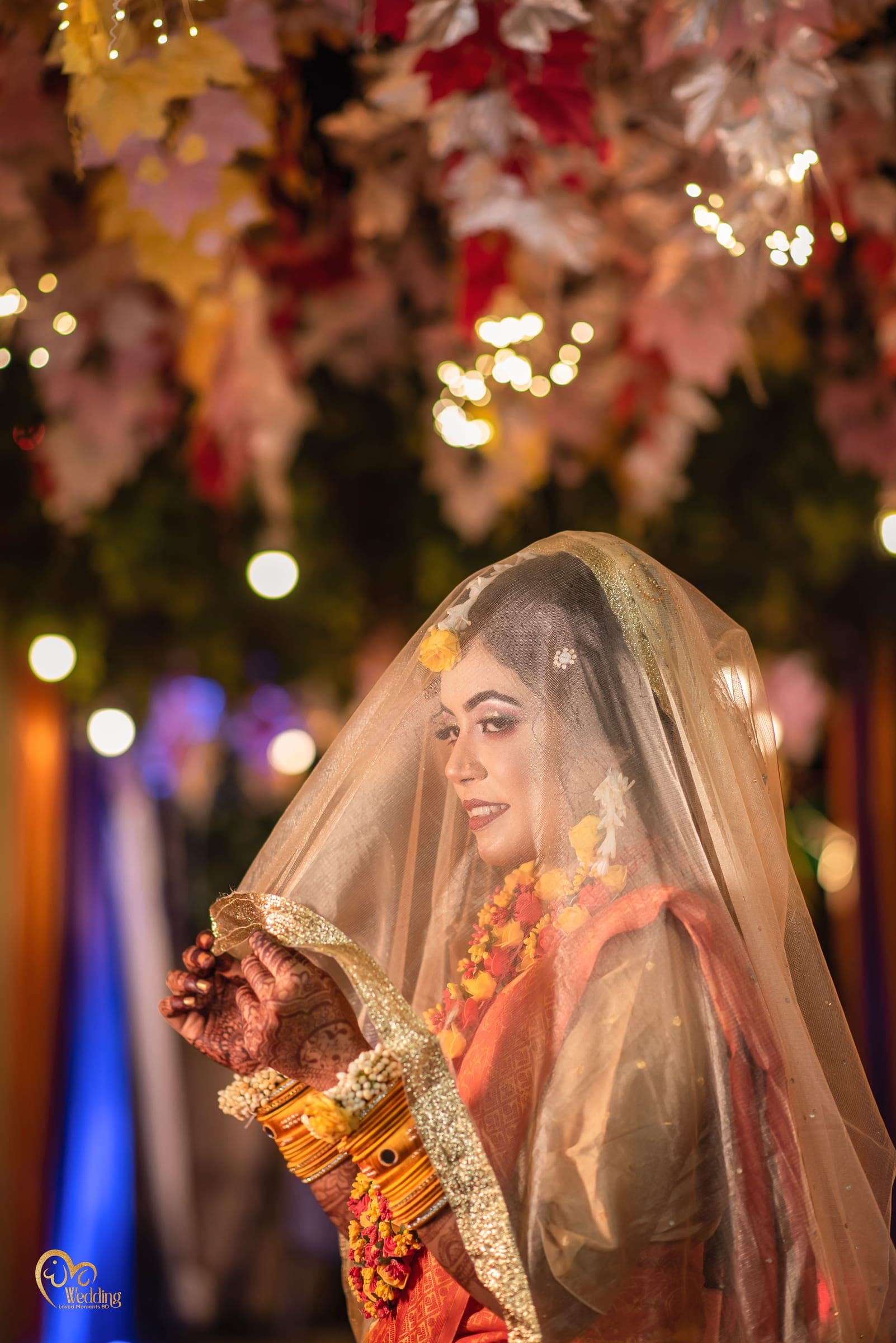 Bride beneath a sheer golden veil with marigold jewellery and warm bokeh lights