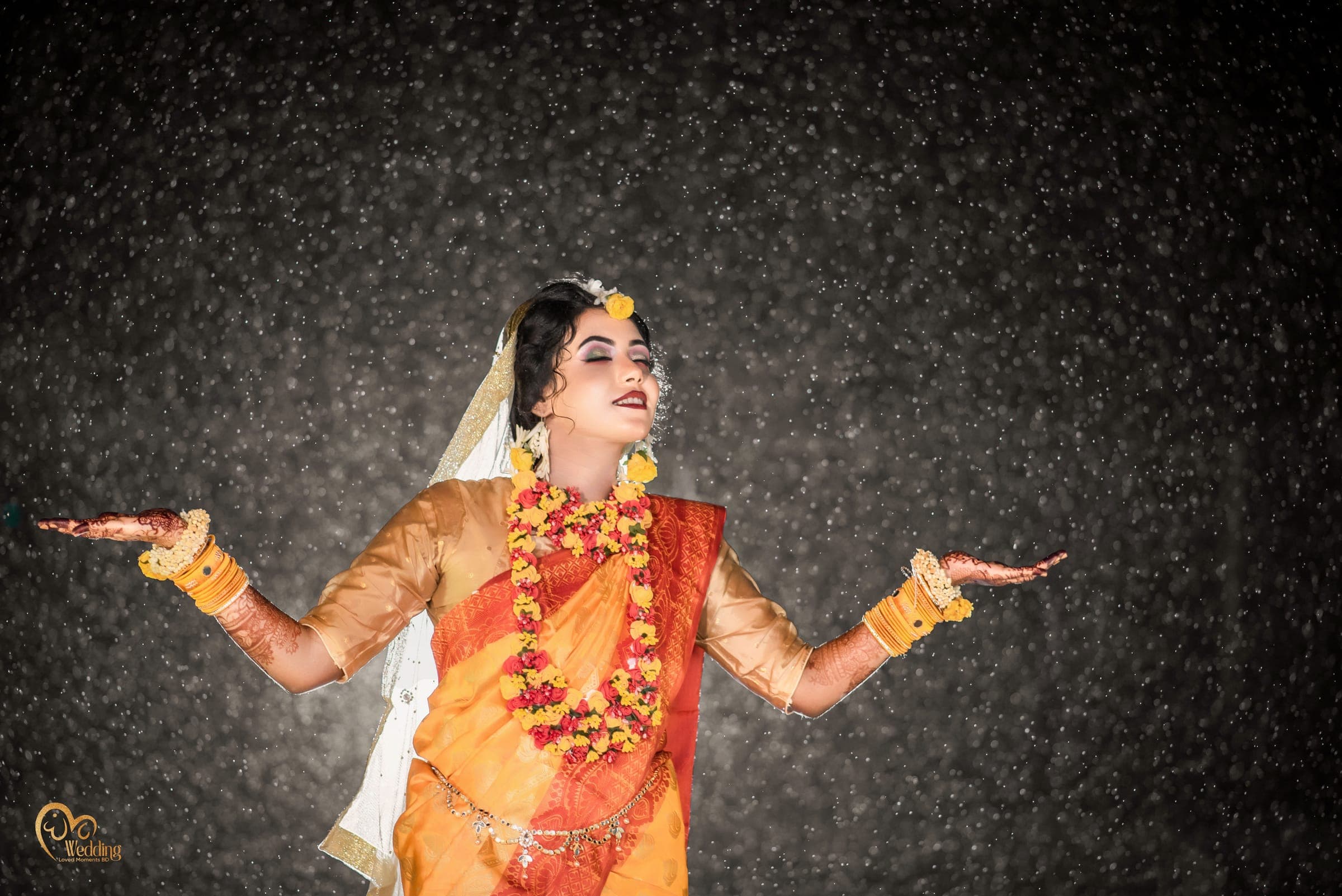 Bride in an orange holud saree with arms outstretched in falling sparkles